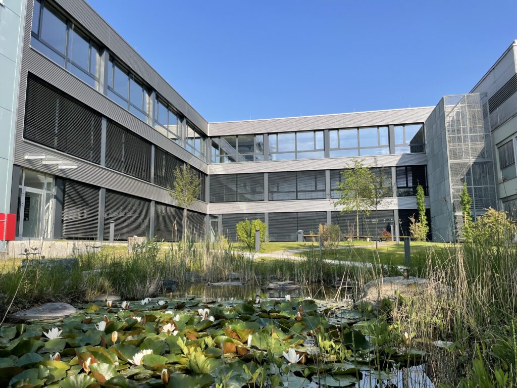 Blick auf einen Gebäudeteil von The Plan Konstanz mit Teich und Begrünung im Vordergrund